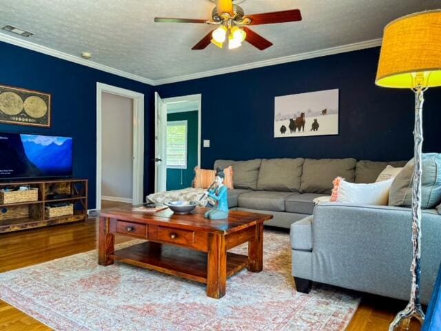 living area featuring visible vents, a ceiling fan, wood finished floors, crown molding, and a textured ceiling