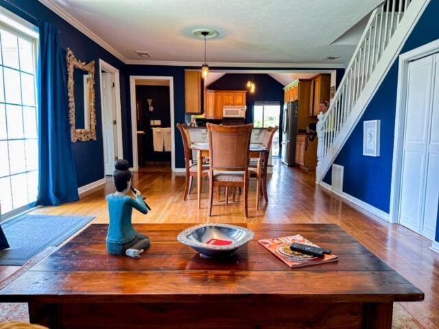 dining room with crown molding, light wood-type flooring, plenty of natural light, and stairway