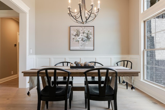 dining area featuring a chandelier, a decorative wall, a wainscoted wall, visible vents, and light wood-type flooring