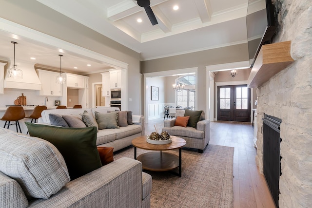 living room with light wood-style flooring, ornamental molding, coffered ceiling, beamed ceiling, and ceiling fan with notable chandelier