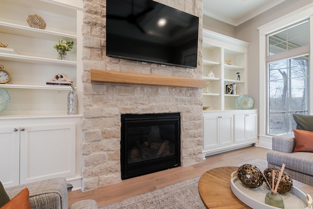 living area with a wealth of natural light, a stone fireplace, ornamental molding, and light wood-style flooring