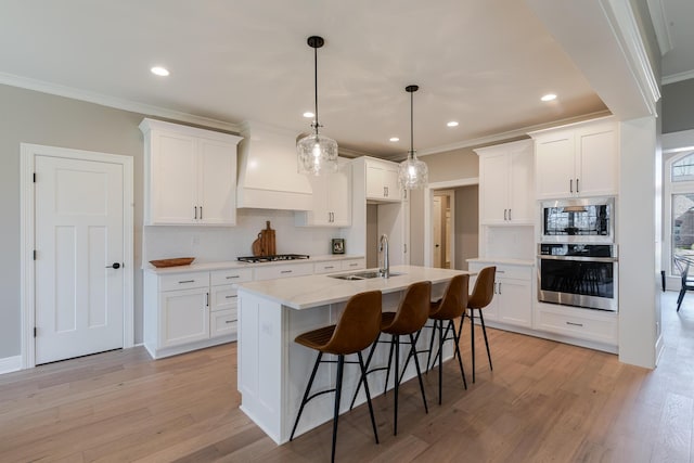 kitchen featuring light wood-style flooring, stainless steel appliances, a sink, ornamental molding, and custom range hood