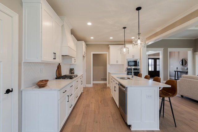 kitchen featuring light wood-style flooring, premium range hood, a breakfast bar, a sink, and appliances with stainless steel finishes