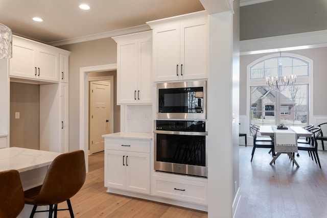 kitchen with light stone counters, a notable chandelier, crown molding, built in microwave, and oven