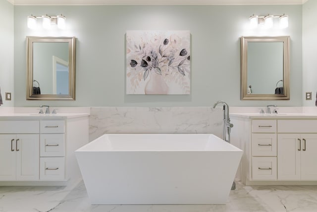 bathroom featuring marble finish floor, a freestanding tub, two vanities, and a sink