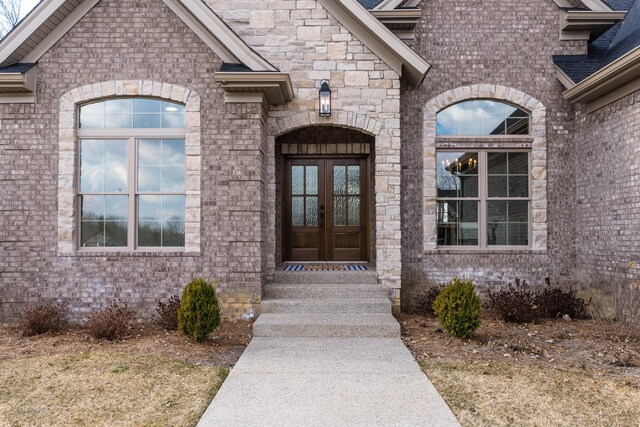 view of exterior entry with stone siding, french doors, and brick siding