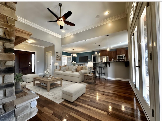 living area with dark wood-style floors, ceiling fan with notable chandelier, baseboards, and crown molding