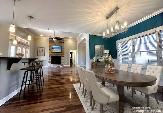 dining area with ceiling fan with notable chandelier, a stone fireplace, baseboards, and wood finished floors