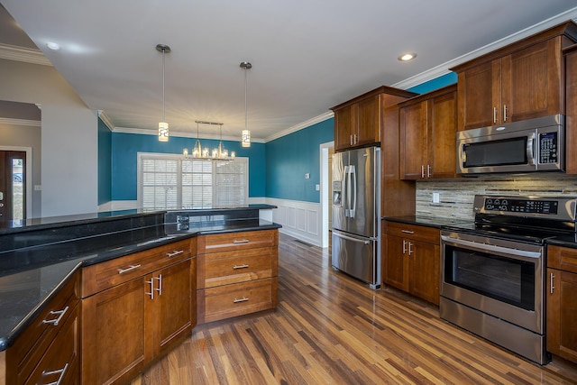 kitchen featuring pendant lighting, a wainscoted wall, dark wood finished floors, stainless steel appliances, and ornamental molding