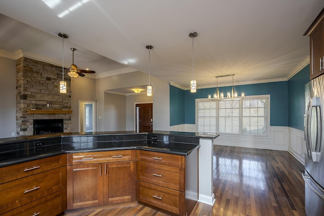 kitchen with a wainscoted wall, crown molding, dark wood-type flooring, stainless steel refrigerator, and pendant lighting