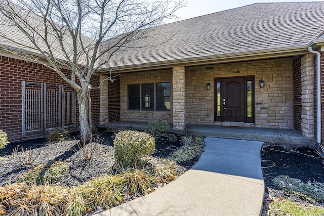 doorway to property with brick siding, stone siding, a porch, and roof with shingles