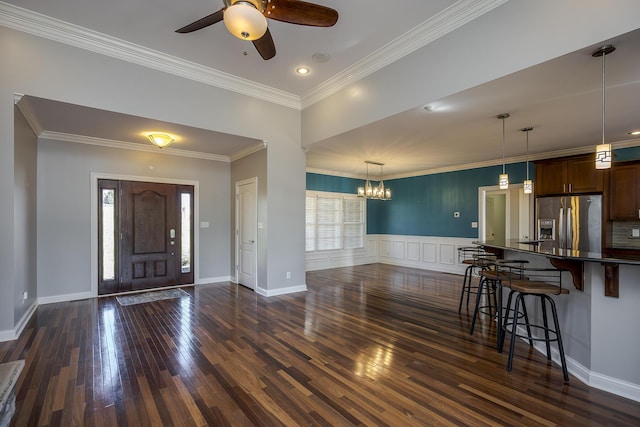 foyer with dark wood finished floors, crown molding, and ceiling fan with notable chandelier