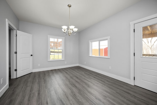 unfurnished dining area with baseboards, an inviting chandelier, and dark wood-style flooring