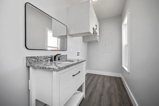 kitchen with a sink, light stone counters, dark wood finished floors, white cabinetry, and baseboards