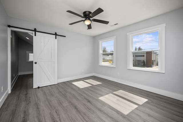 unfurnished bedroom featuring a ceiling fan, wood finished floors, visible vents, baseboards, and a barn door