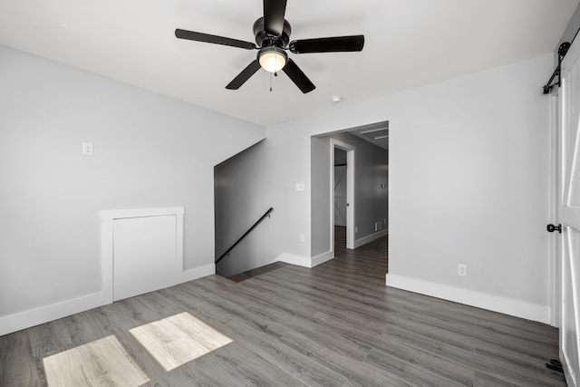 empty room with ceiling fan, baseboards, a barn door, and wood finished floors