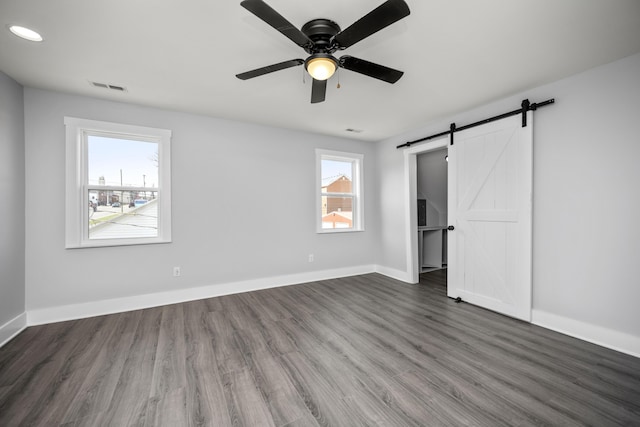 unfurnished bedroom with wood finished floors, baseboards, visible vents, ceiling fan, and a barn door