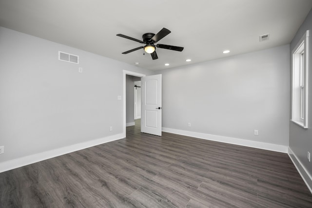 empty room featuring dark wood-type flooring, baseboards, visible vents, and ceiling fan