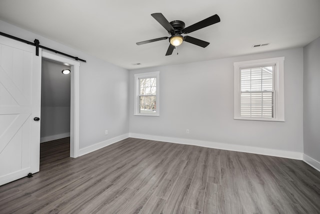 unfurnished room with a barn door, wood finished floors, baseboards, and ceiling fan