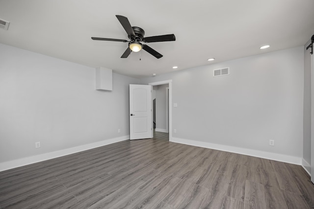 spare room with baseboards, wood finished floors, ceiling fan, and a barn door