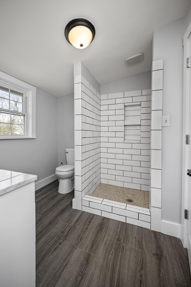 bathroom featuring baseboards, tiled shower, toilet, and wood finished floors