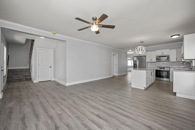 unfurnished living room with stairway, crown molding, light wood-style floors, and a ceiling fan