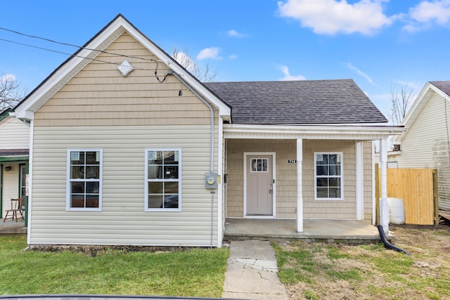 bungalow-style house featuring covered porch, fence, a front lawn, and roof with shingles