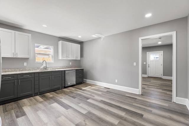 kitchen with baseboards, stainless steel dishwasher, a sink, and white cabinets