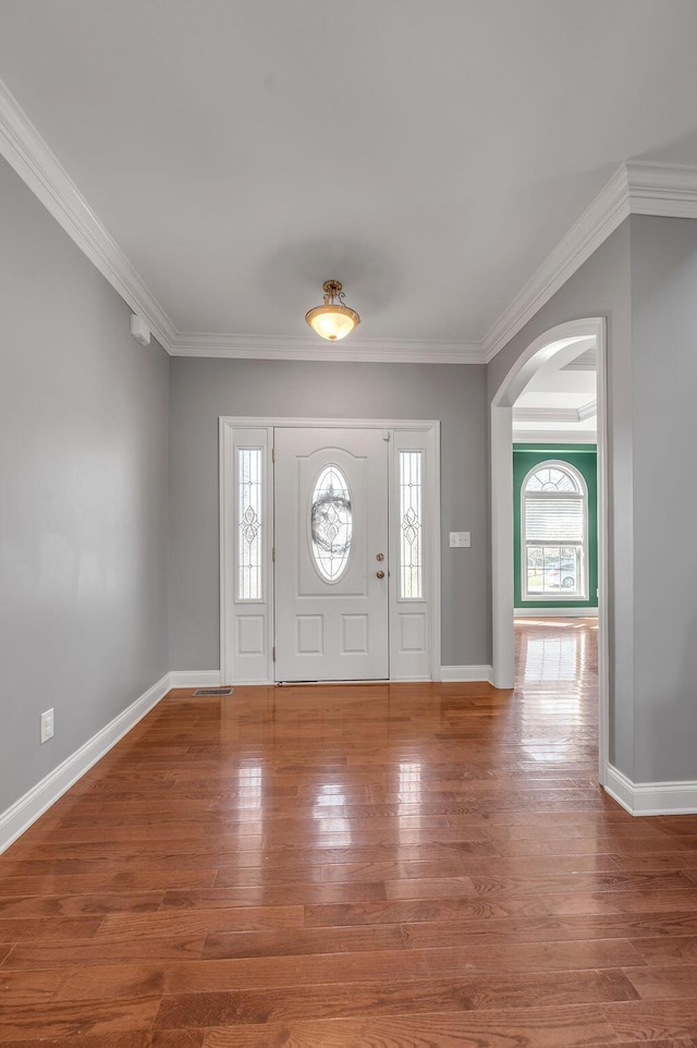 entryway with arched walkways, crown molding, and wood finished floors