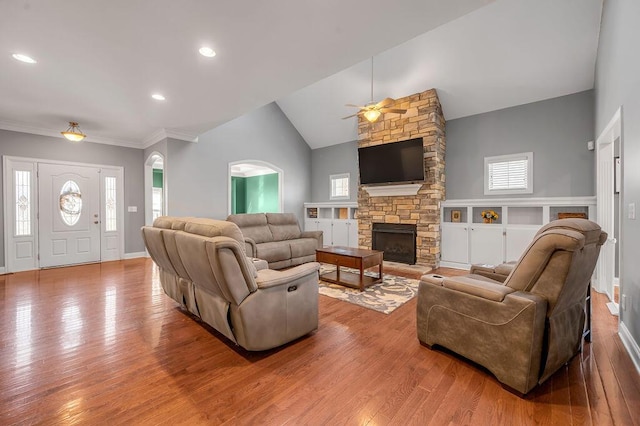 living area featuring lofted ceiling, a stone fireplace, wood finished floors, and a healthy amount of sunlight