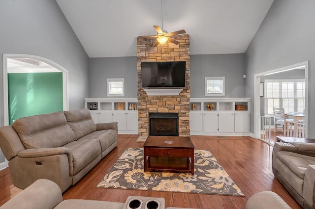 living room with high vaulted ceiling, ceiling fan, a stone fireplace, and wood finished floors