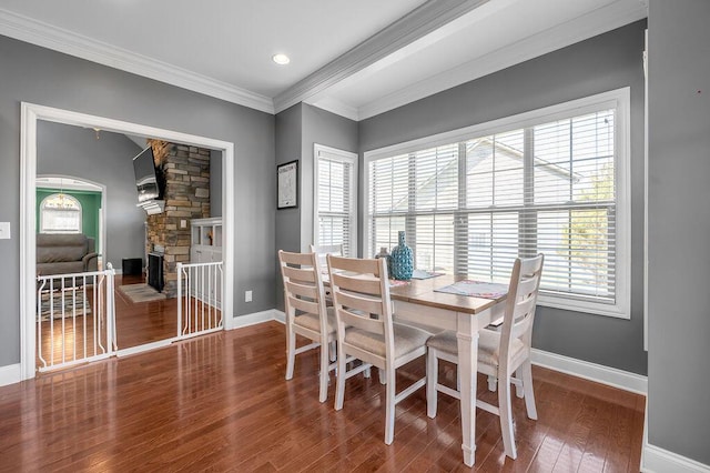 dining space with crown molding, a stone fireplace, wood finished floors, and baseboards