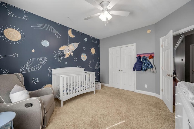 bedroom featuring a crib, baseboards, an accent wall, carpet, and a closet