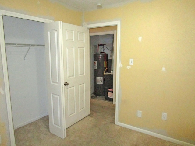 unfurnished bedroom with light carpet, baseboards, a closet, and electric water heater