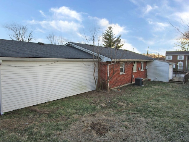 rear view of property featuring a shingled roof, cooling unit, brick siding, and a lawn