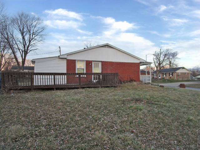 rear view of house with a deck, a lawn, and brick siding