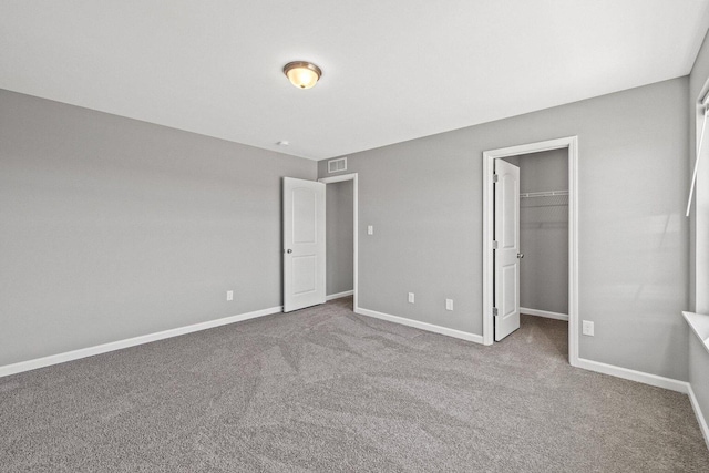 unfurnished bedroom featuring carpet floors, visible vents, baseboards, and a walk in closet