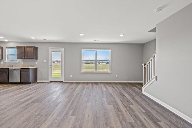 unfurnished living room featuring stairs, a healthy amount of sunlight, wood finished floors, and baseboards