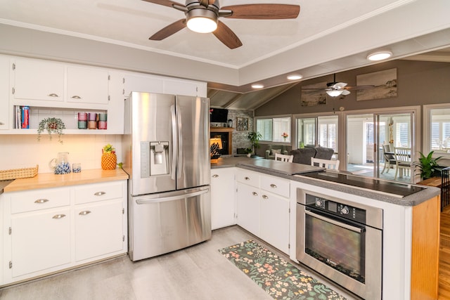 kitchen with a ceiling fan, stainless steel appliances, a peninsula, a fireplace, and lofted ceiling