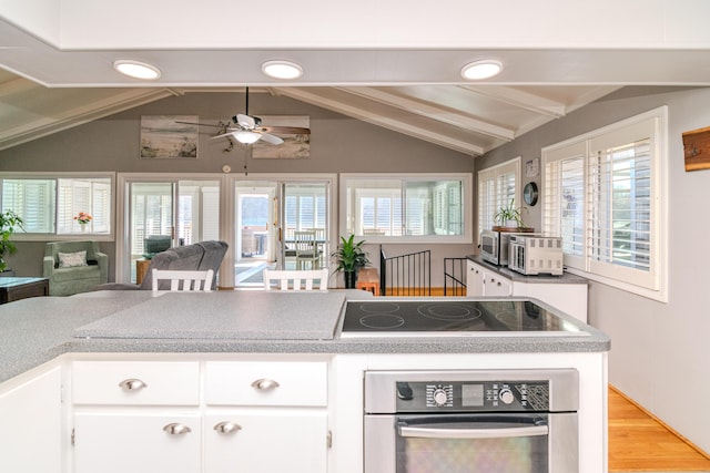 kitchen featuring a healthy amount of sunlight, vaulted ceiling with beams, black electric stovetop, stainless steel oven, and a ceiling fan