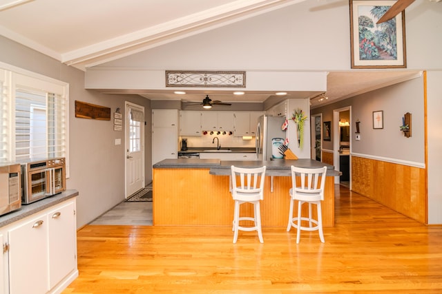 kitchen with lofted ceiling, freestanding refrigerator, a sink, wainscoting, and dark countertops