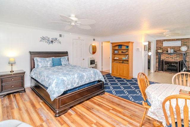 bedroom with a brick fireplace, heating unit, wood finished floors, and visible vents