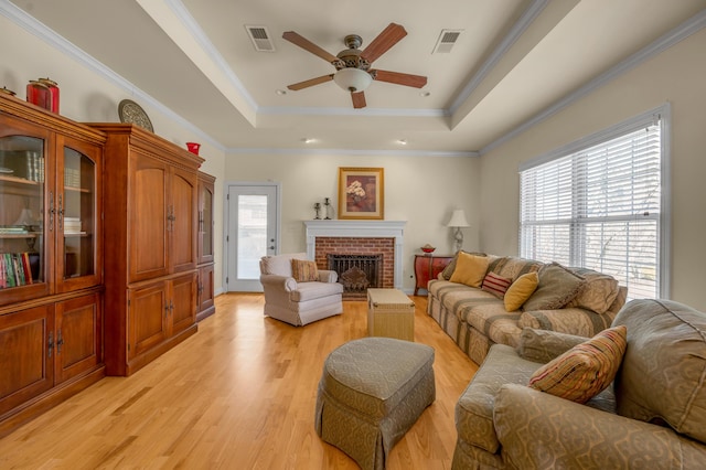 living area with light wood finished floors, visible vents, ornamental molding, a tray ceiling, and a fireplace