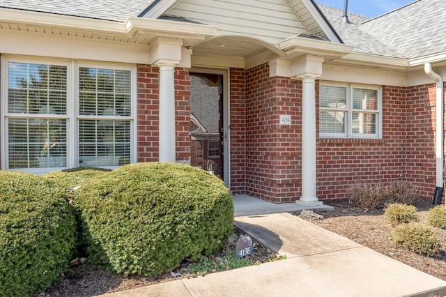 entrance to property featuring a shingled roof and brick siding