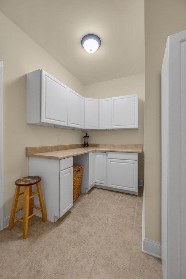 kitchen with light countertops, white cabinets, built in desk, and baseboards