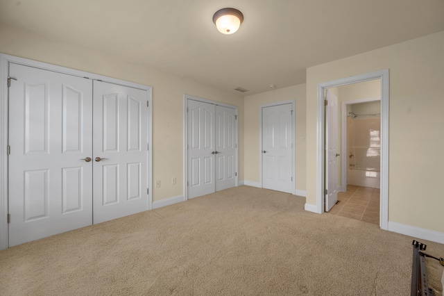 unfurnished bedroom with light carpet, two closets, visible vents, and baseboards