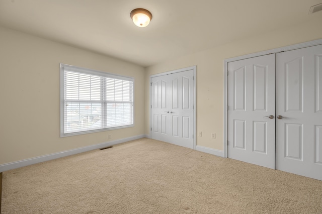 unfurnished bedroom with baseboards, carpet floors, visible vents, and multiple closets