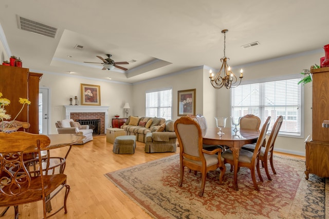 dining room with light wood-style flooring, a brick fireplace, a raised ceiling, and visible vents