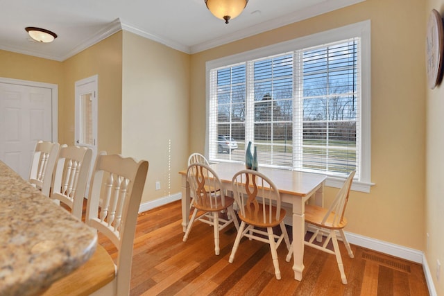 dining space with light wood finished floors, ornamental molding, visible vents, and baseboards