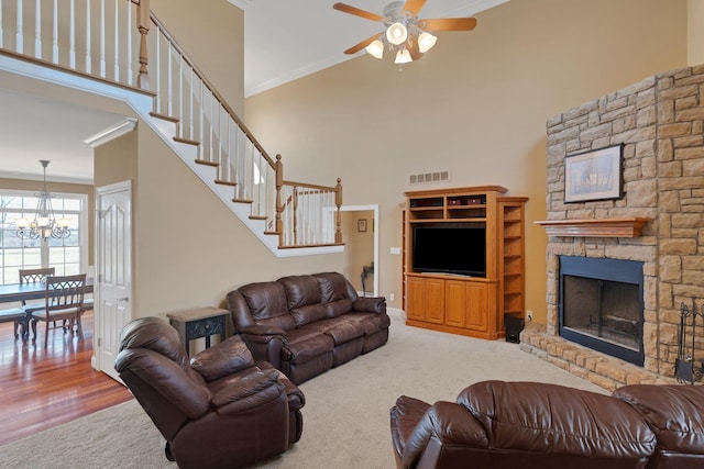 carpeted living area featuring visible vents, ornamental molding, stairs, a high ceiling, and ceiling fan with notable chandelier